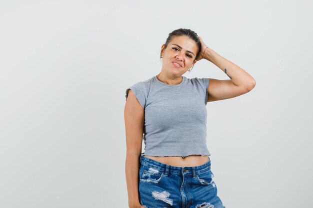 Señorita en camiseta, pantalones cortos posando mientras sostiene la mano en la cabeza y se ve bien