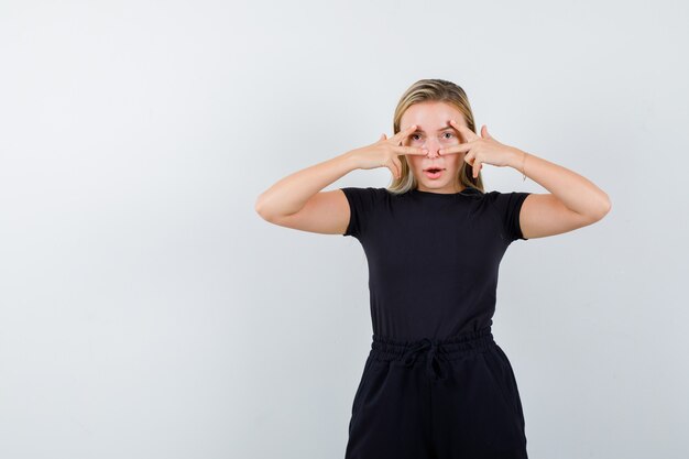 Señorita en camiseta, pantalones mostrando signos de victoria en los ojos y mirando confiada, vista frontal.