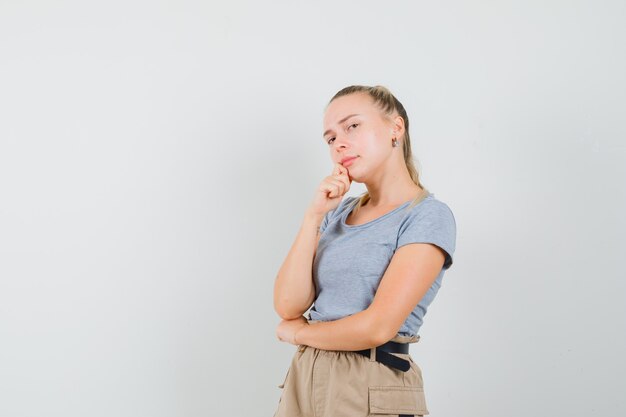 Señorita en camiseta y pantalones de pie en pose de pensamiento y mirando sensible