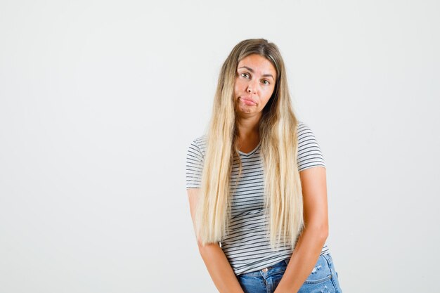 Señorita en camiseta de pie y mirando molesto, vista frontal.