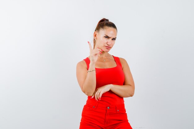 Señorita en camiseta roja, pantalón rojo apuntando hacia arriba y mirando serio, vista frontal.