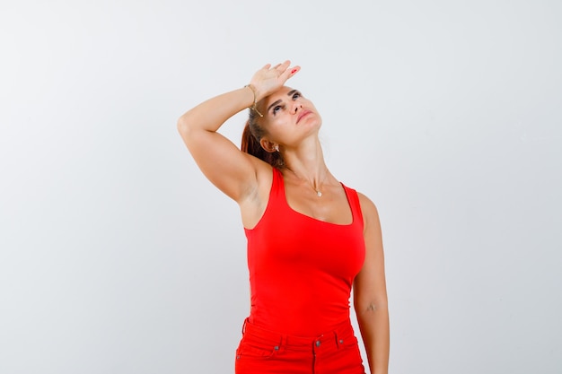 Foto gratuita señorita en camiseta roja, pantalón rojo con la mano en la frente y aspecto cansado, vista frontal.