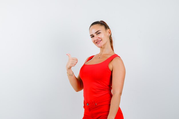 Señorita en camiseta roja, pantalón rojo mostrando el pulgar hacia arriba y mirando complacido, vista frontal.