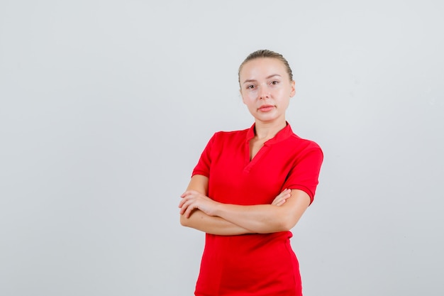 Señorita en camiseta roja de pie con los brazos cruzados y mirando confiado