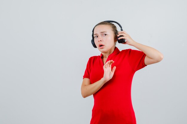 Señorita en camiseta roja quitándose los auriculares con gesto de parada y mirando asustado