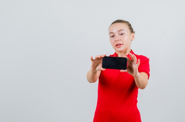 Señorita en camiseta roja tomando fotos en el teléfono móvil