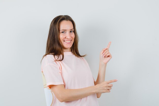 Señorita en camiseta rosa apuntando hacia arriba y a un lado y mirando jovial