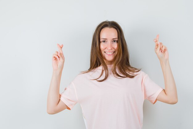 Señorita en camiseta rosa manteniendo los dedos cruzados y mirando feliz