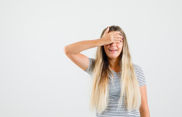 Señorita en camiseta sosteniendo la mano sobre sus ojos y mirando emocionado, vista frontal.