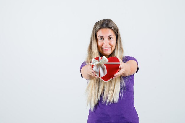 Señorita en camiseta violeta mostrando caja de regalo y mirando feliz, vista frontal.