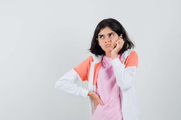 Señorita en chaqueta, camisa rosa sosteniendo la mano en la barbilla y mirando nerviosa