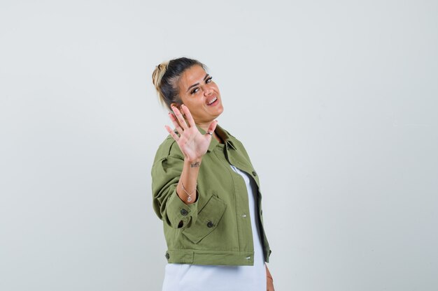 Señorita en chaqueta de camiseta mostrando gesto de parada y mirando alegre