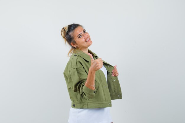 Señorita en chaqueta de camiseta mostrando el pulgar hacia arriba tirando de la chaqueta y mirando confiado