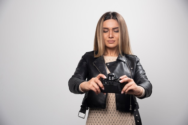 Señorita en chaqueta de cuero negro tomando fotos con la cámara de manera seria y profesional.