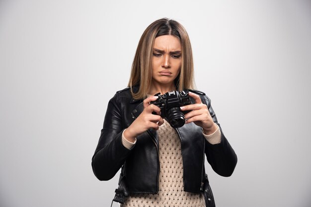 Señorita en chaqueta de cuero negro tomando fotos con la cámara de manera seria y profesional