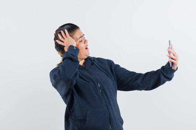 Señorita en chaqueta haciendo videollamadas y mirando enfocado