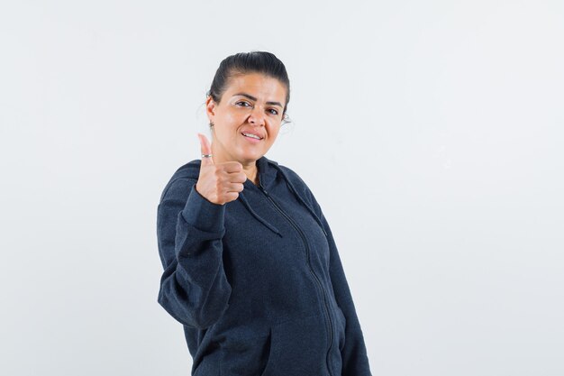 Señorita en chaqueta mostrando el pulgar hacia arriba y mirando contento