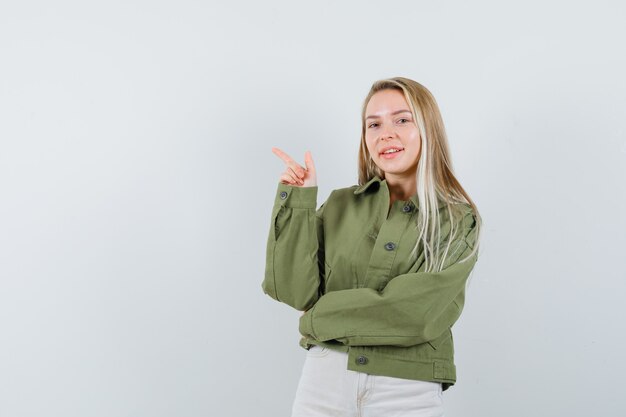 Señorita con chaqueta, pantalones apuntando a la esquina superior izquierda y mirando alegre, vista frontal.