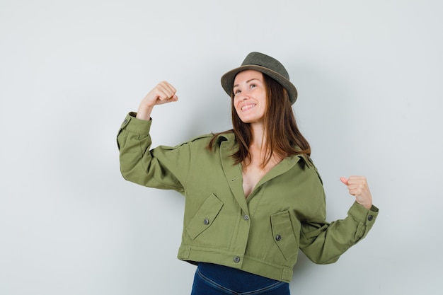 Señorita en chaqueta pantalones sombrero mostrando gesto de ganador y mirando feliz