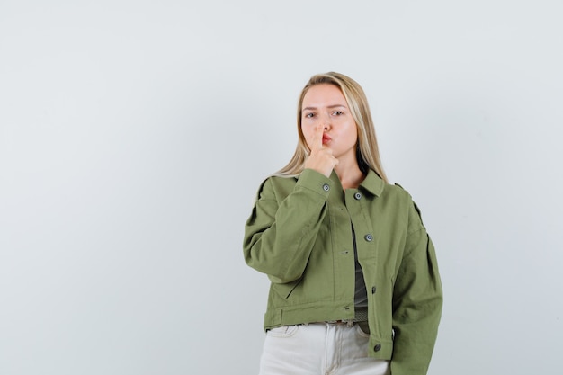 Señorita en chaqueta, pantalones tocándose la nariz con el dedo y luciendo hermosa vista frontal.