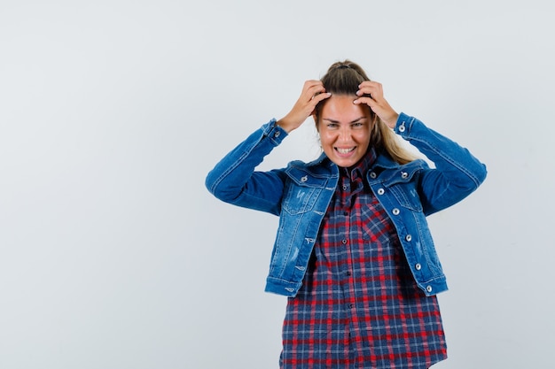 Señorita cogidos de la mano en la cabeza en camisa, chaqueta y mirando feliz. vista frontal.