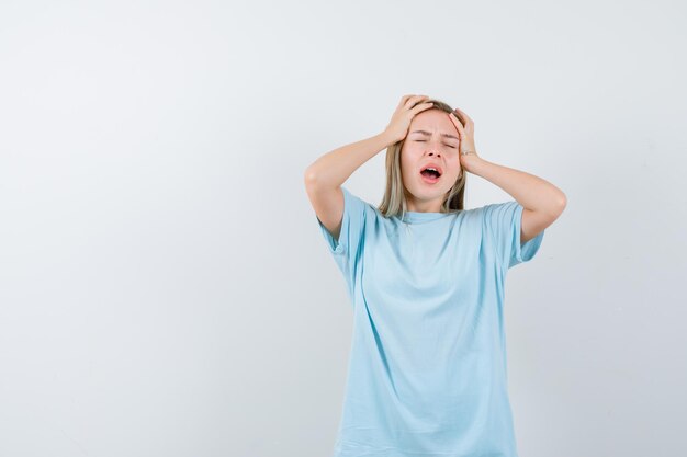 Señorita cogidos de la mano en la cabeza en camiseta y mirando molesto aislado