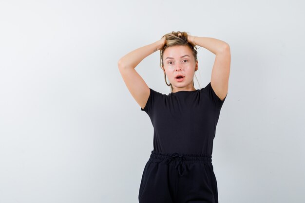 Señorita cogidos de la mano en la cabeza en camiseta, pantalón y mirando pensativo. vista frontal.