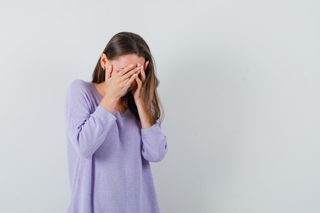 Señorita cogidos de la mano en la cara en camisa casual y con cara de tristeza