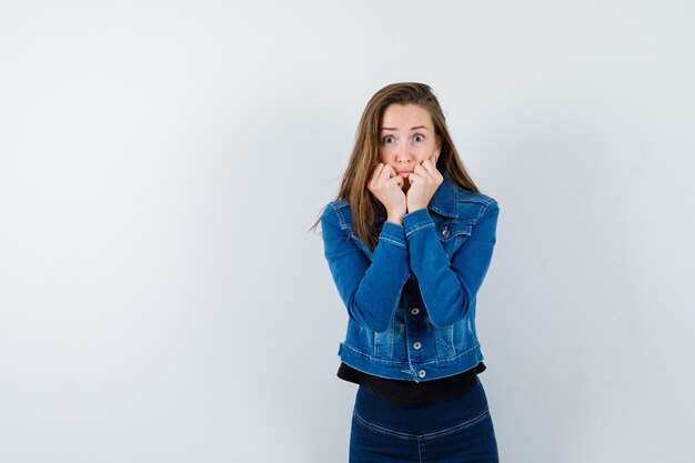 Señorita cogidos de la mano cerca de la boca en blusa, chaqueta y mirando asustado, vista frontal.