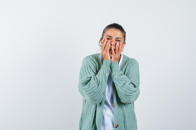 Señorita cogidos de la mano en las mejillas en camiseta, chaqueta y mirando positivo