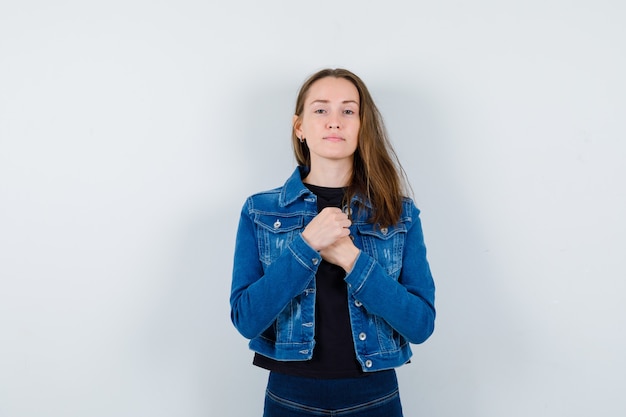 Señorita cogidos de la mano en el pecho con blusa, chaqueta y aspecto sensato.