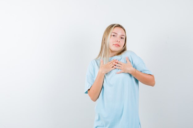 Señorita cogidos de la mano en el pecho en camiseta y mirando confiada. vista frontal.