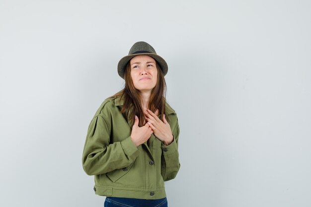 Señorita cogidos de la mano en el pecho mientras fruncía el ceño en chaqueta pantalones sombrero