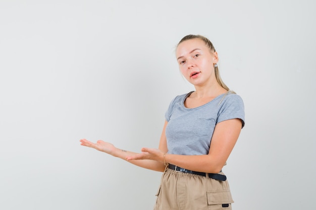 Señorita dando la bienvenida o mostrando algo en camiseta y pantalones y mirando alegre