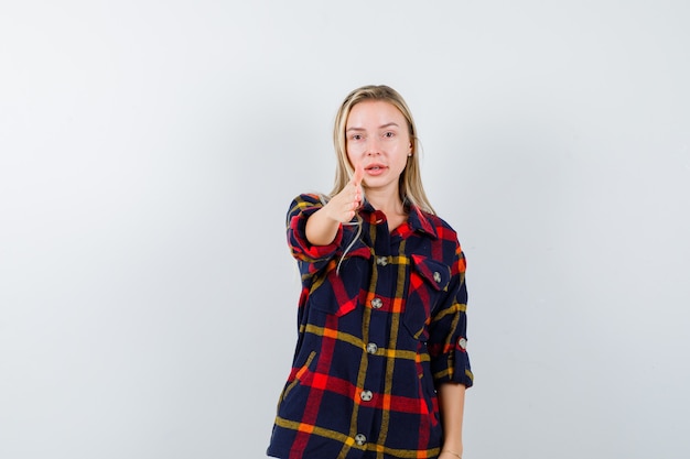 Señorita dando la mano para saludar en camisa a cuadros y mirando confiada. vista frontal.