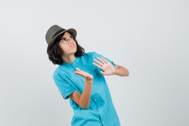 Foto gratuita señorita defendiendo con las manos en camisa azul, sombrero y mirando alarmado.