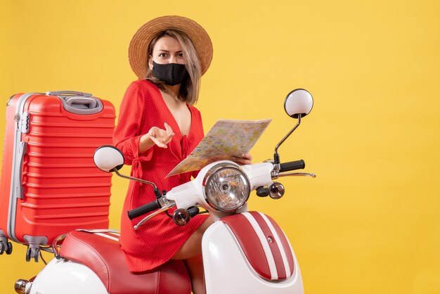 Señorita desconcertada en vestido rojo en ciclomotor con mapa