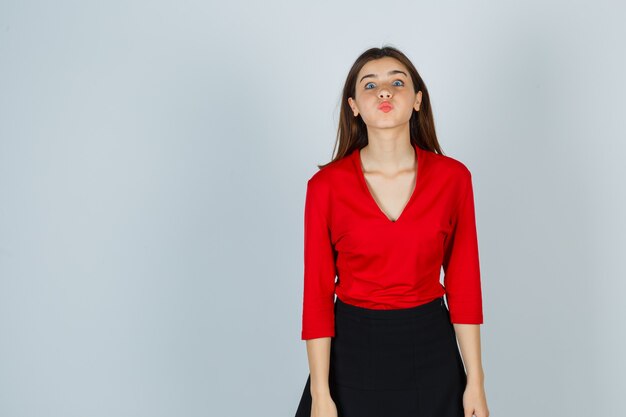 Señorita enviando beso con labios fruncidos en blusa roja, falda y luciendo bonita