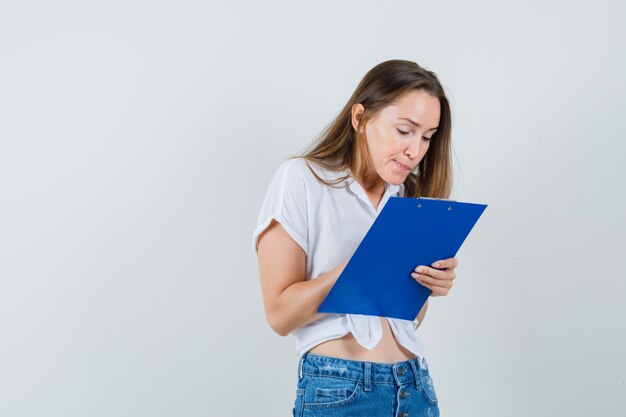 Señorita escribiendo algo en el portapapeles en blusa blanca, vista frontal.