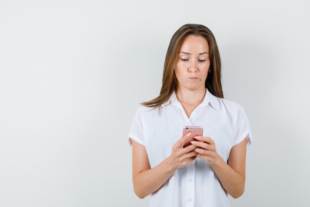 Señorita escribiendo algo en el teléfono en blusa blanca y mirando desconcertado