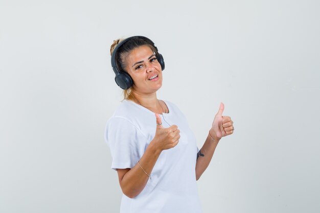 Señorita escuchando música, mostrando el doble pulgar hacia arriba en la vista frontal de la camiseta.