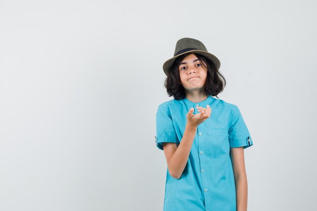 Señorita expresando su sentimiento con la mano en camisa azul, sombrero y aspecto emocional.