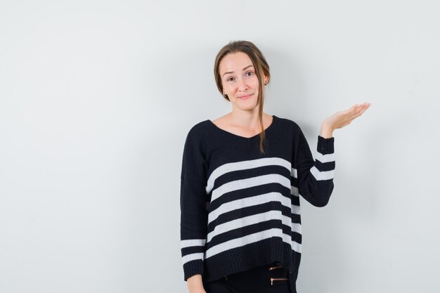 Señorita extendiendo la palma a un lado en camisa casual y mirando positivo