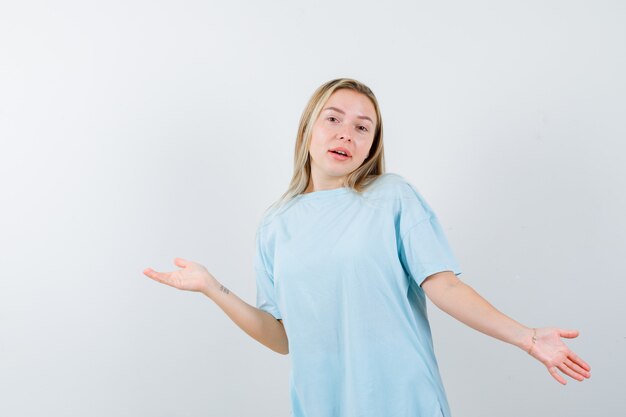 Señorita extendiendo las palmas a un lado en camiseta y mirando impotente. vista frontal.