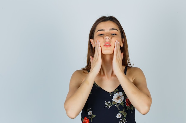 Foto gratuita señorita fingiendo frotar crema para la piel en las mejillas en blusa y mirando relajado, vista frontal.