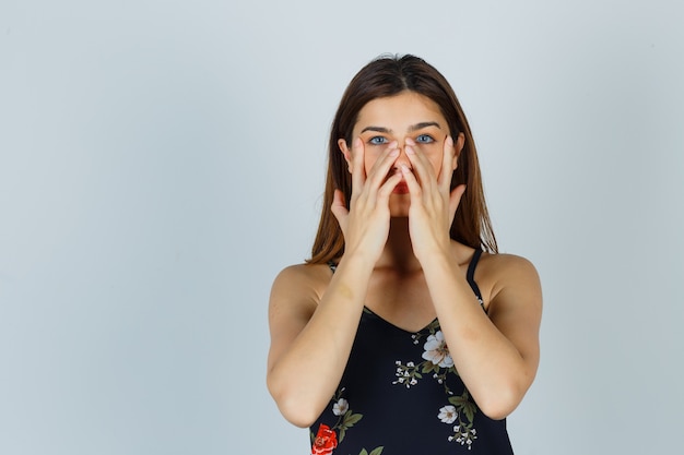 Señorita fingiendo frotar la mascarilla alrededor de la zona de la nariz en blusa y luciendo encantadora. vista frontal.