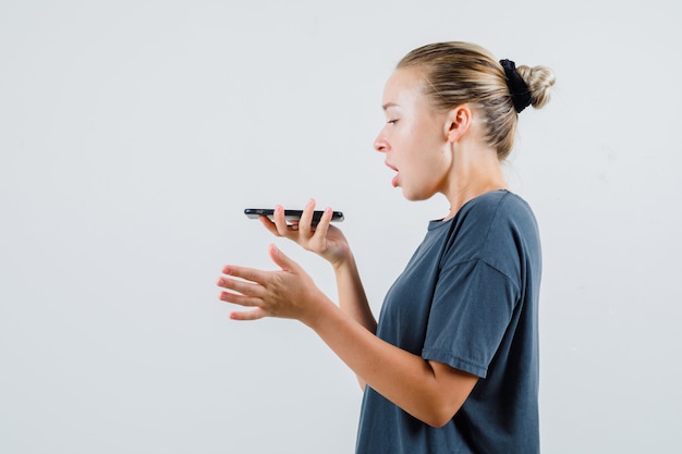 Señorita grabando mensaje de voz en el teléfono móvil en camiseta gris.