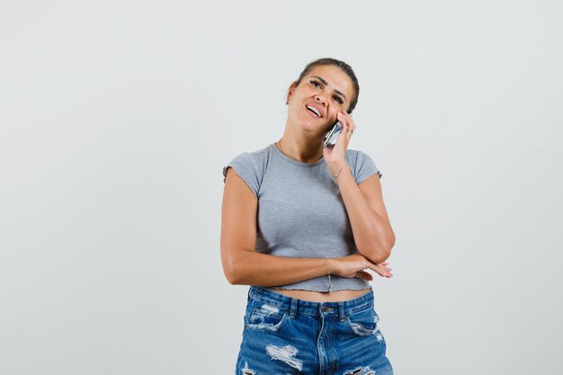 Señorita hablando por teléfono móvil en camiseta, pantalones cortos y con aspecto optimista.