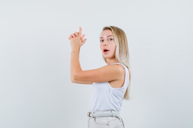 Señorita haciendo gesto de pistola en blusa blanca y mirando listo