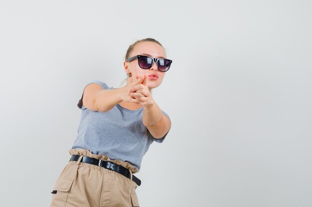 Señorita haciendo signo de pistola de dedo en camiseta y pantalón y mirando confiado